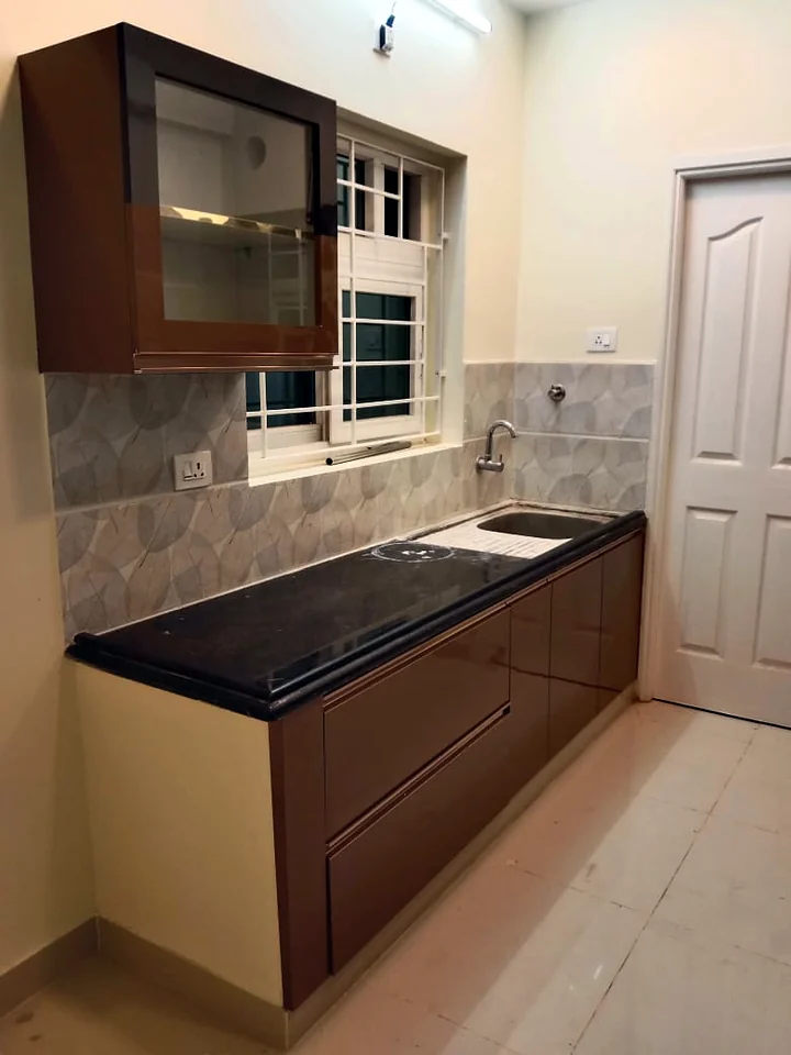 Compact modular kitchen with walnut-finish cabinets and glass-front wall unit for a Chennai apartment
