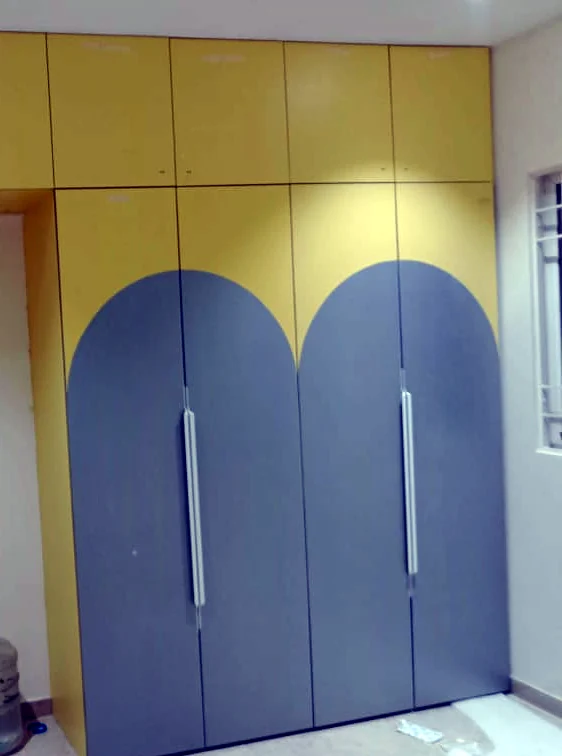 Yellow and grey bedroom wardrobe with arch-shaped shutters and loft storage by Wood Crops, Chennai